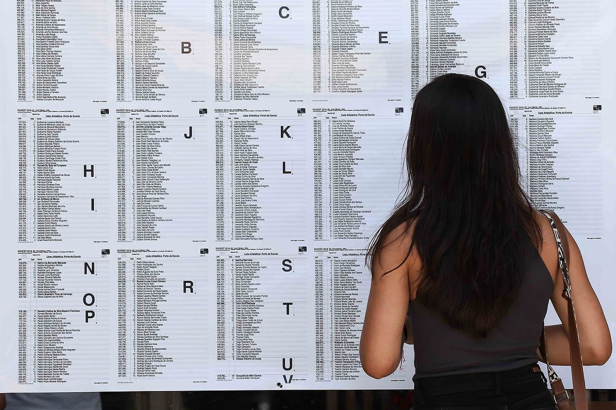 Menina de costas olhando uma parede em que há várias listas com nomes; Fuvest 2024: lista de aprovados em 1ª chamada é liberada