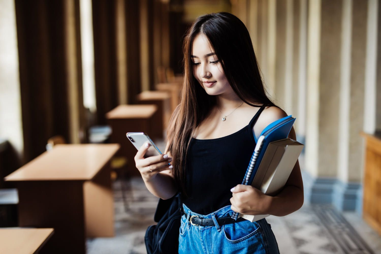 Mulher olhando o celular e segurando livros; direito no Sisu 2024: confira as menores notas de corte