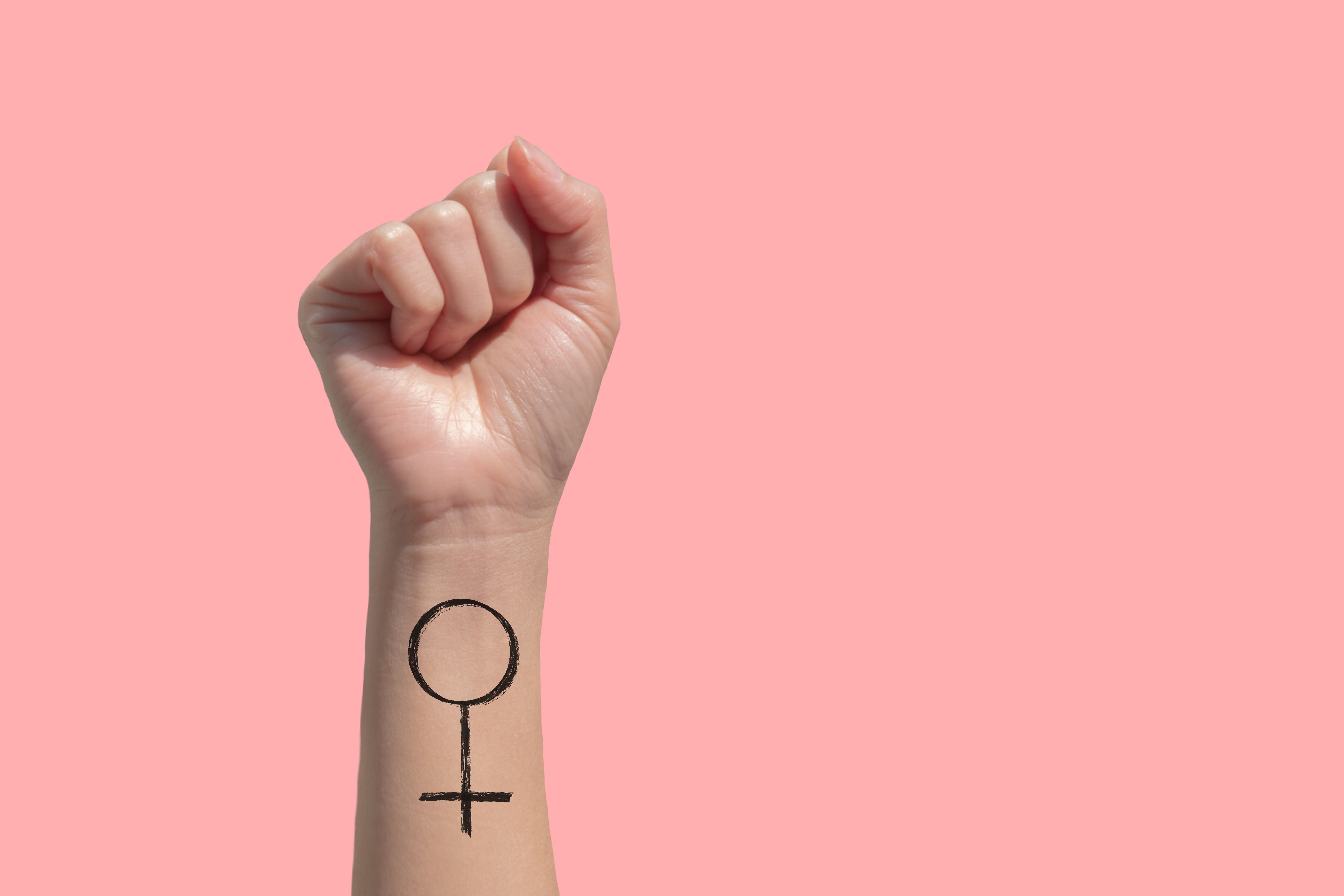 mão com o punho fechado e o símbolo do feminismo desenhado em um fundo rosa