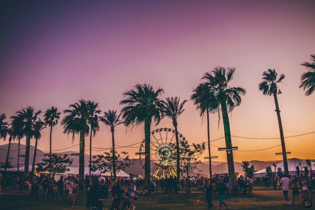 Pessoas andando no lugar onde é realizado o Coachella durante o pôr-do-sol, ao fundo, uma roda-gigante; Coachella 2024: o que significa, quando acontece e como assistir