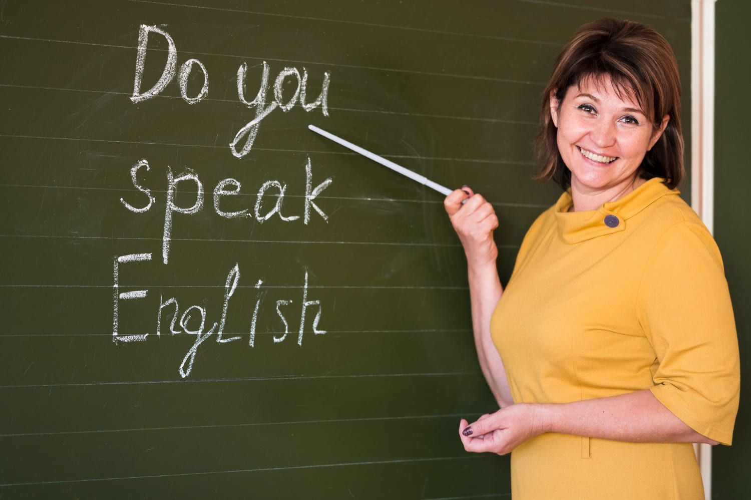 Professora de inglês ensinando sobre os níveis de inglês aponta para uma lousa, onde está escrito do you speak english