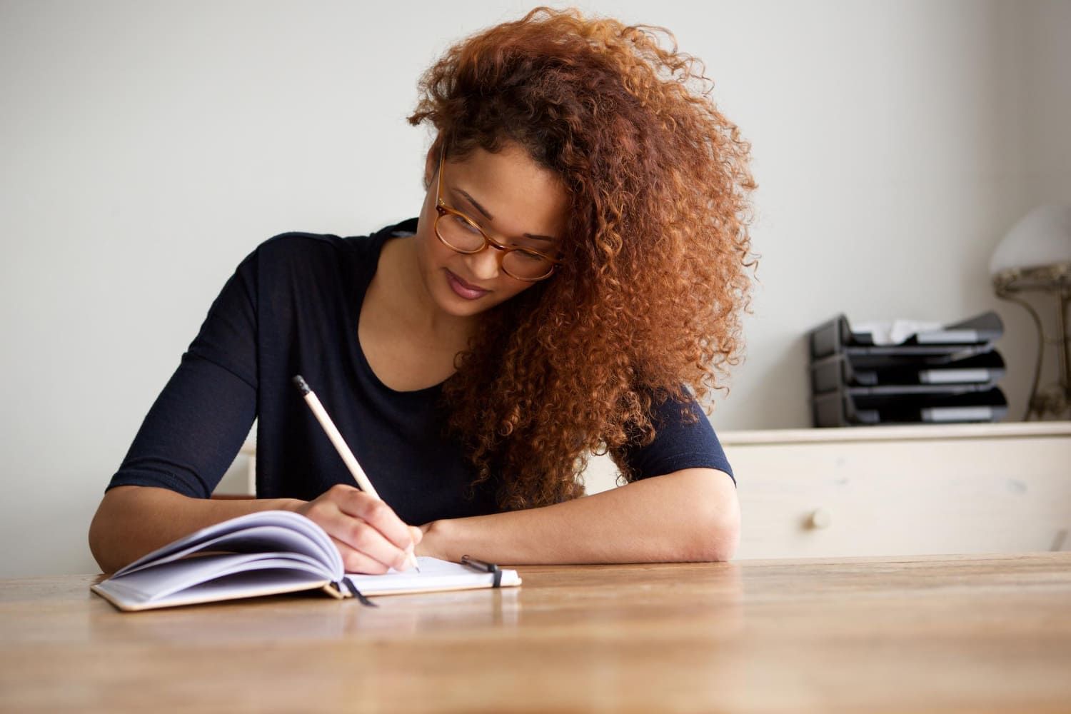 Jovem sentada em uma mesa escrevendo em um caderno e aprendendo a como fazer uma redação dissertativa-argumentativa para o Enem e outros vestibulares