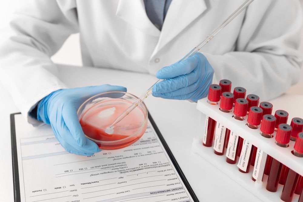 Profissional de biologia está no processo de identificar a tipagem sanguínea de umpaciente, e para isso está colhendo amostras dos tubos de coleta de sangue dele em um laboratório.