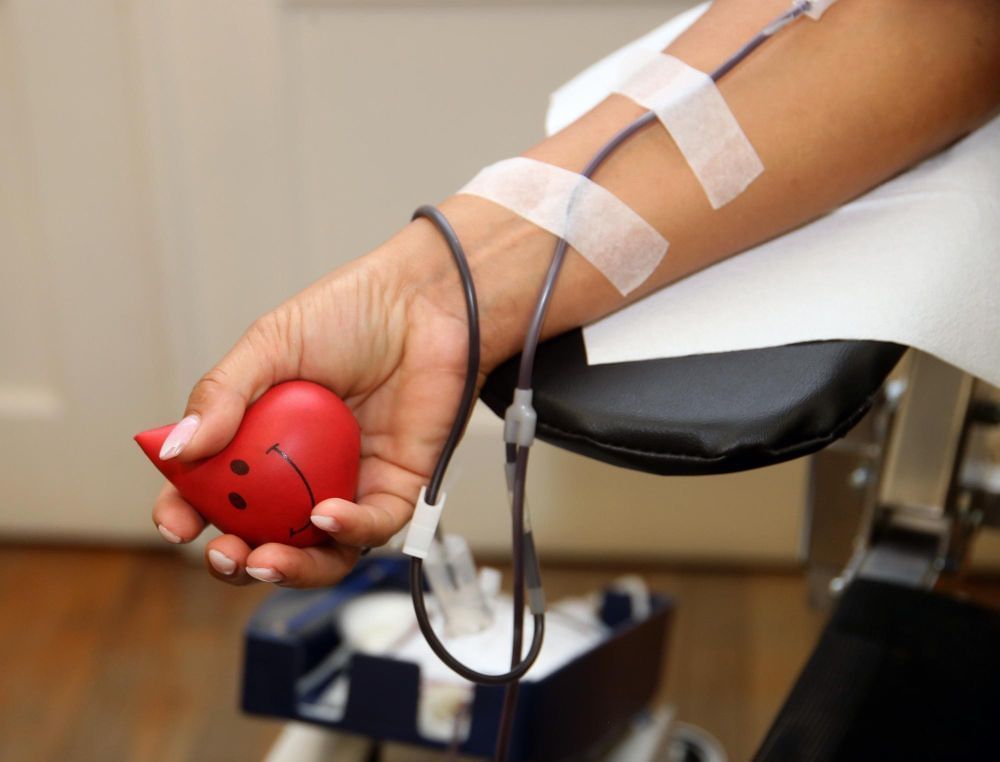 Uma pessoa em processo de doação de sangue está sentada apertando a bolinha utilizada para melhorar o fluxo sanguíneo.