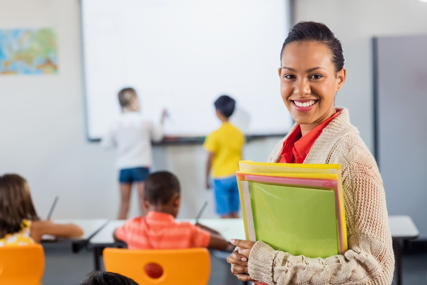 Pedagoga sorrindo em frente a uma sala de aula no dia Dia do Pedagogo; veja 15 melhores frases para homenagear