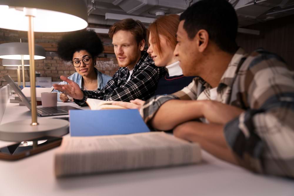 Grupo de alunos adultos estão observando em um computador opções de cursos de extensão universitária enquanto conversam.