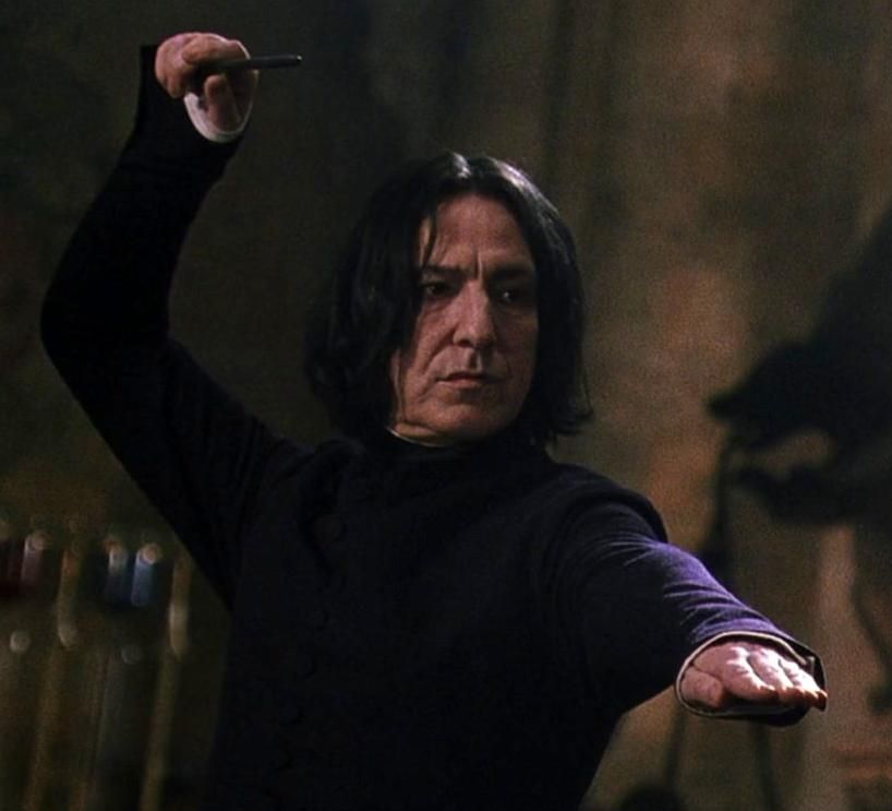 Snape com roupa preta e apontando sua varinha para alguém 