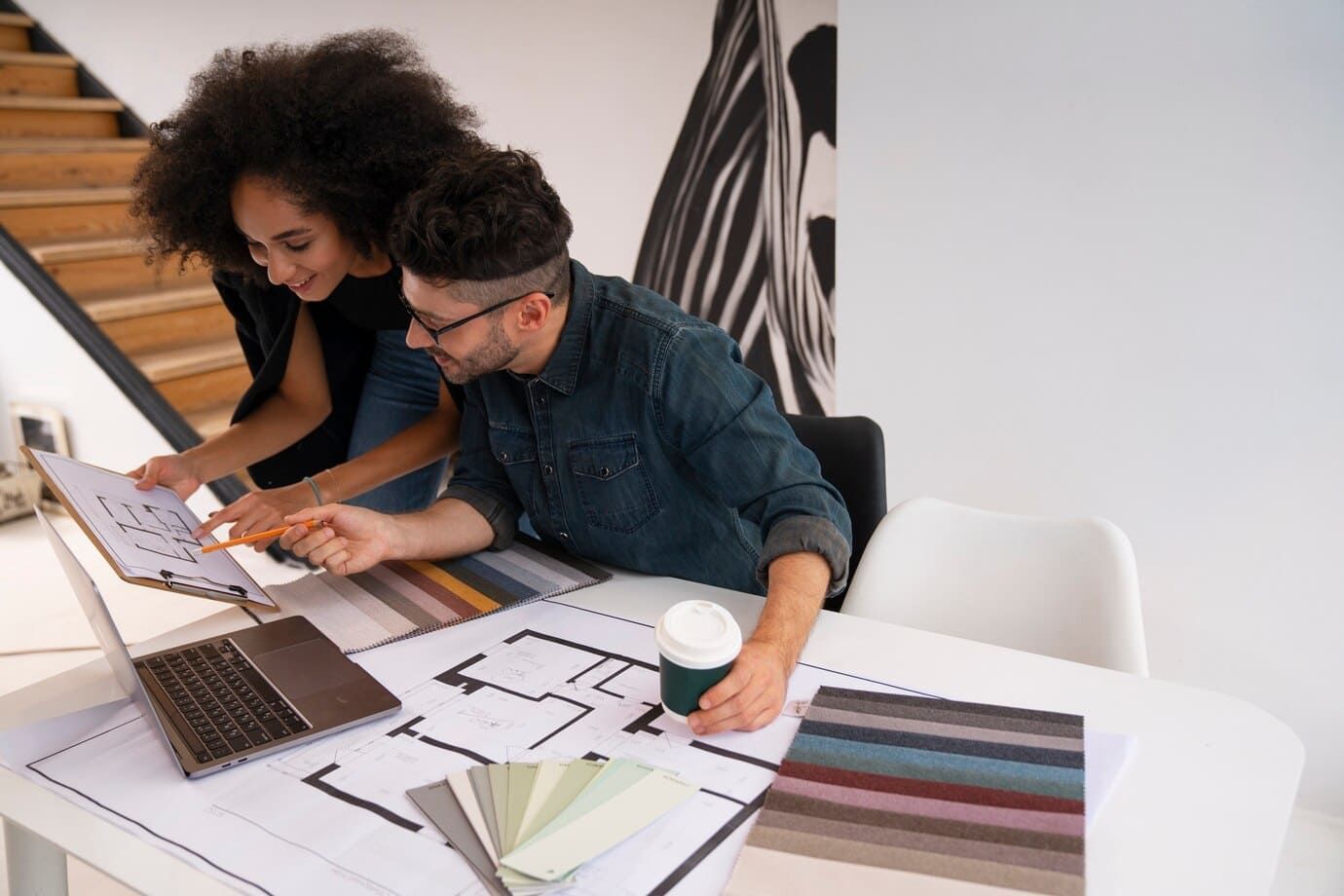 Dois profissionais de design de interiores, um homem branco e uma mulher negra trabalhando juntos olhando plantas e escolhendo cores para organização do espaço