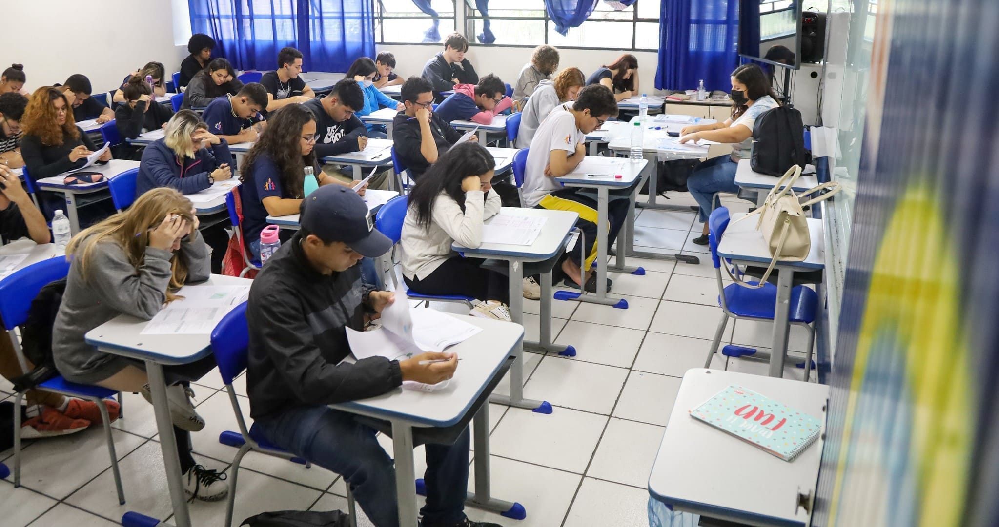 Estudantes em sala de aula sentados nas carteiras fazendo prova