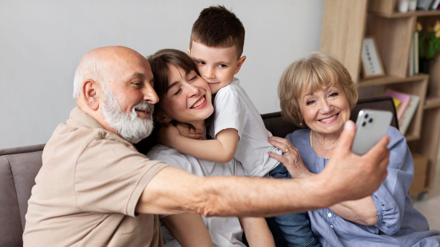 Avós com seu neto e filha tirando selfie sorrindo em família; confira as melhores frases para homenagear no Dia dos Avós