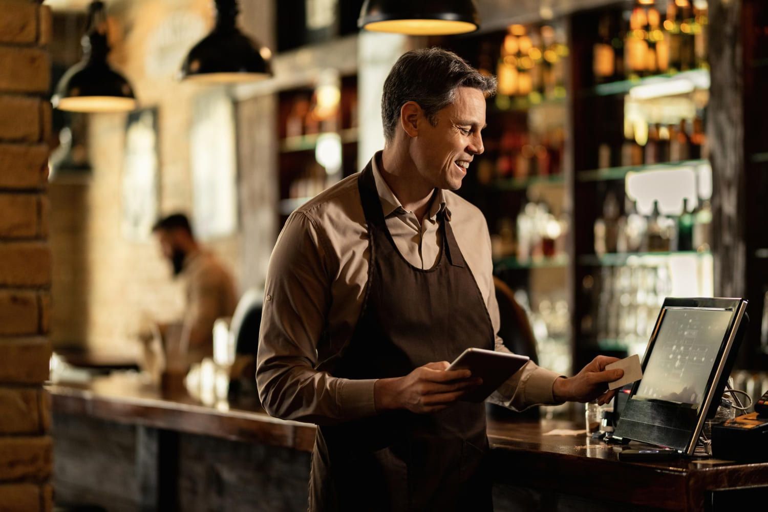  Barista feliz adicionando um pedido à caixa registradora enquanto trabalha em um bar; confira tudo sobre Técnico em Serviços de Restaurante e Bar