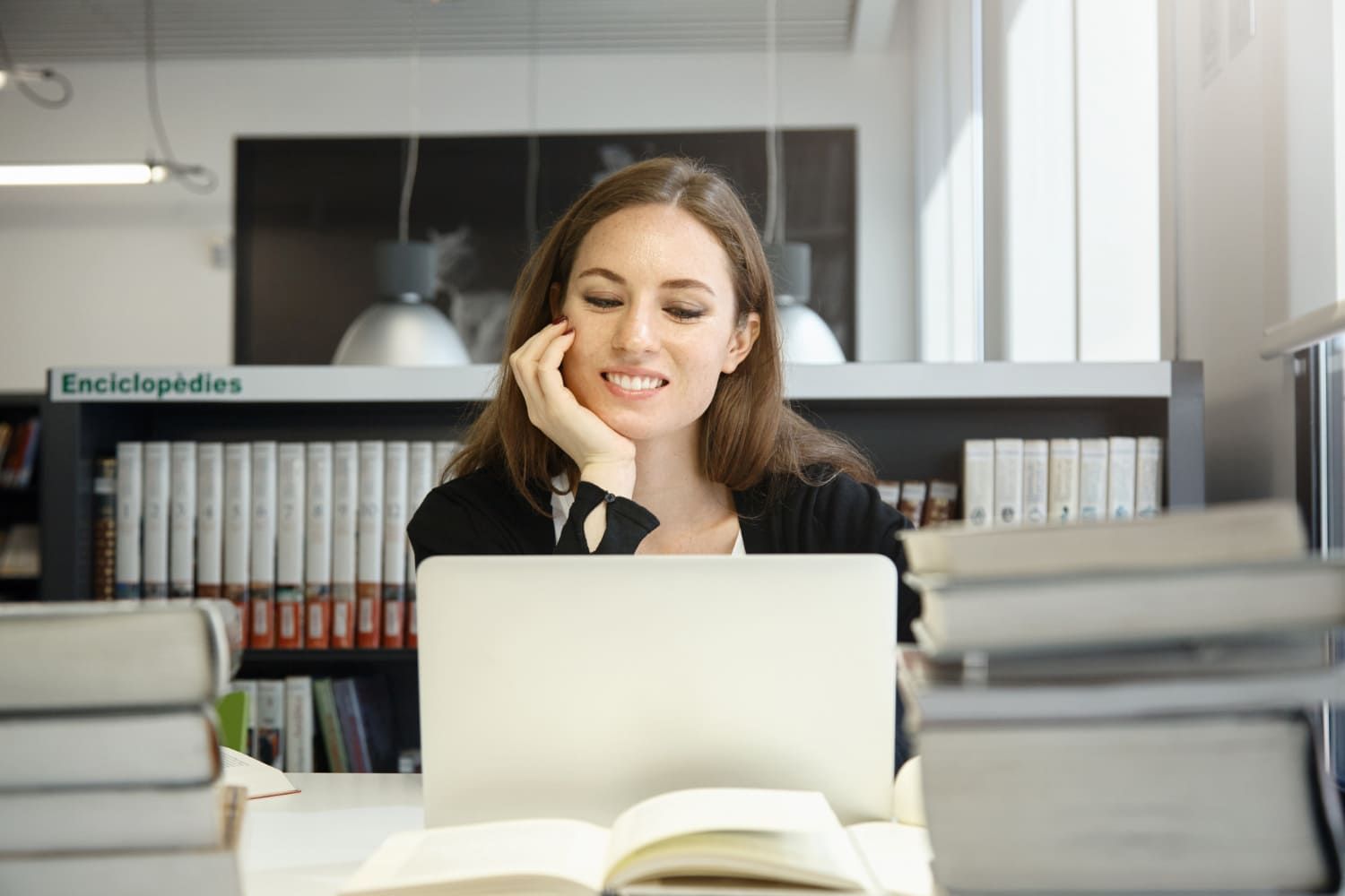 Mulher sorrindo ao olhar para a tela de computador buscando as melhores pós-graduações para entrar no meio do ano