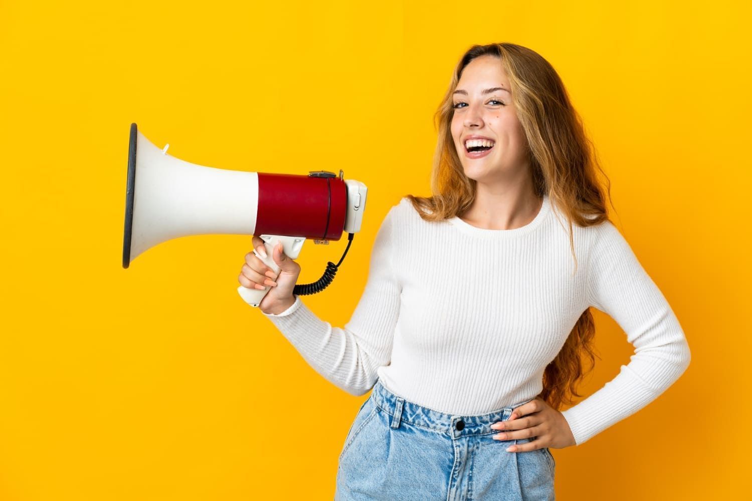 Mulher loira sorrindo segurando um megafone para anunciar que o período de complementação das inscrições do Fies começou