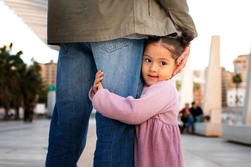 menina abraçada na perna do pai