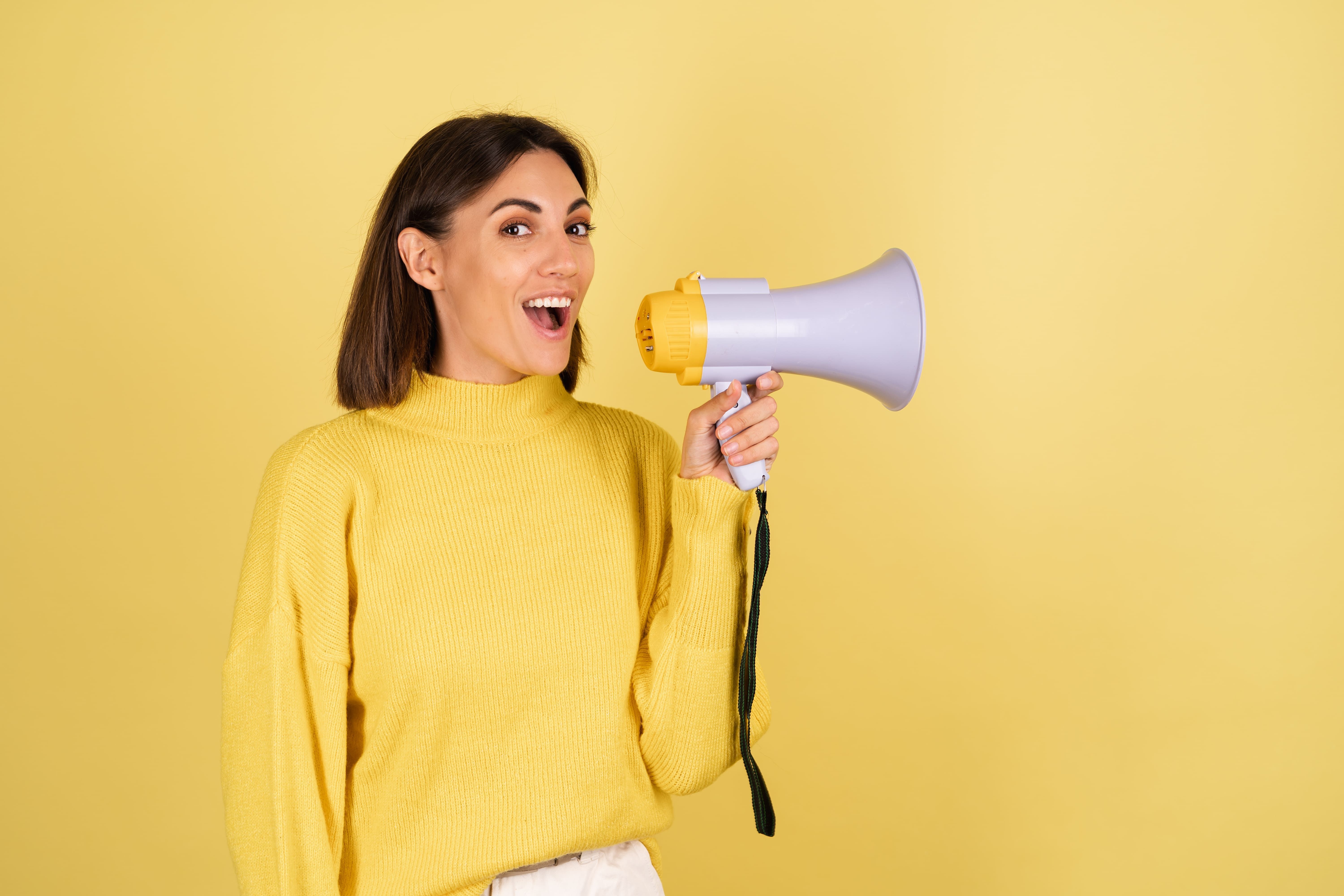 mulher segurando megafone em fundo amarelo