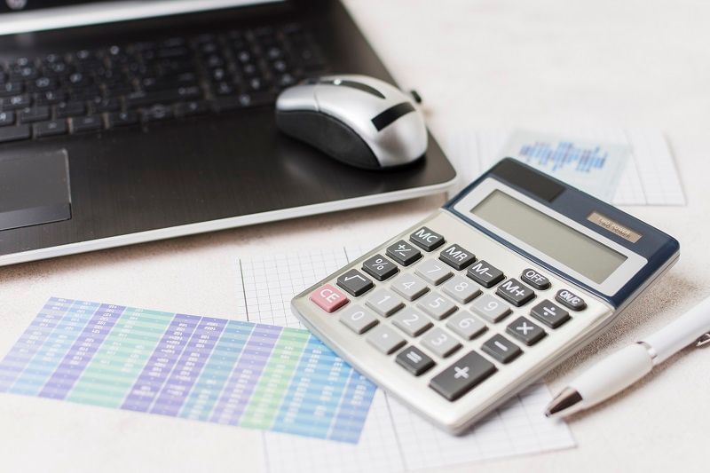 Imagem possui elemntos da prática contábil: computador, mouse, caneta e calculadora.