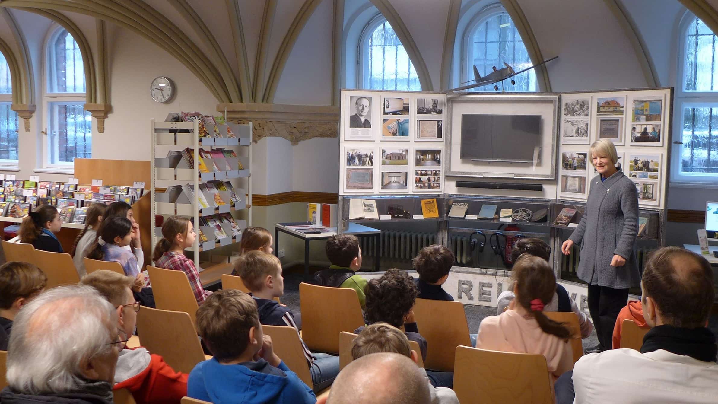 Sabine Reichwein mit der Ausstellung &uuml;ber ihren Vater vor Sch&uuml;lerInnen in einer Bibliothek
