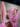 A close up of a sculptural artwork. We see a large pink paper cone had with streamers and a gold sun attached in the foreground and a blurry object in the background