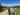 A group of people are spread out walking on a path through a wooded landscape. It's a sunny day and they are carriyng day rucksacks and chatting