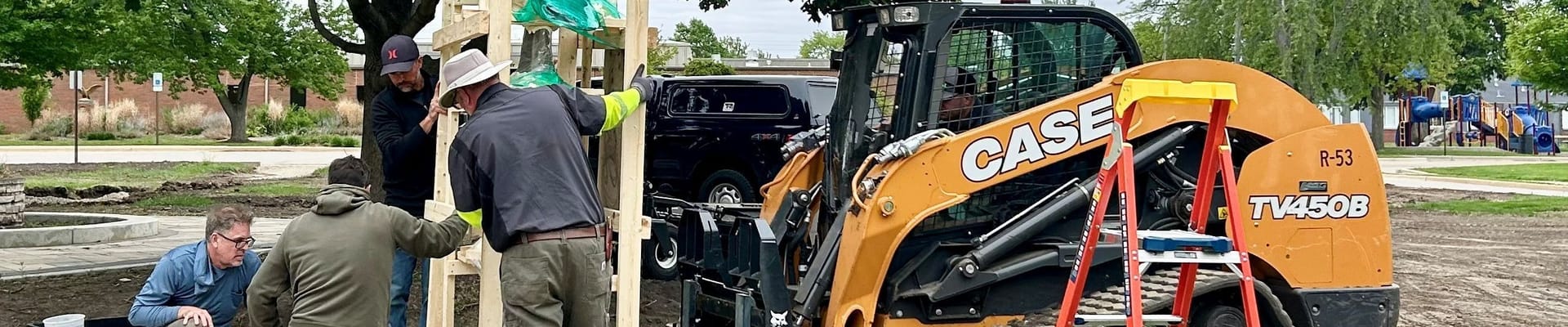 Men guide a crated piece of artwork as a forklift moves it to a concrete plaza.