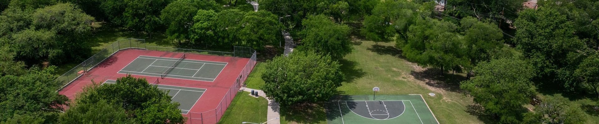 Greenspace with basketball court and tennis courts with green trees all around
