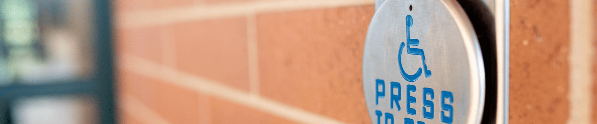 photo of a press to open button with the official handicap symbol mounted on the outside of a building made with red brick.