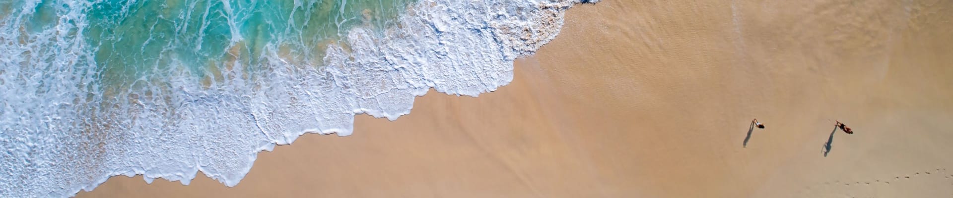 Aerial photo of the ocean and two people walking on the shore