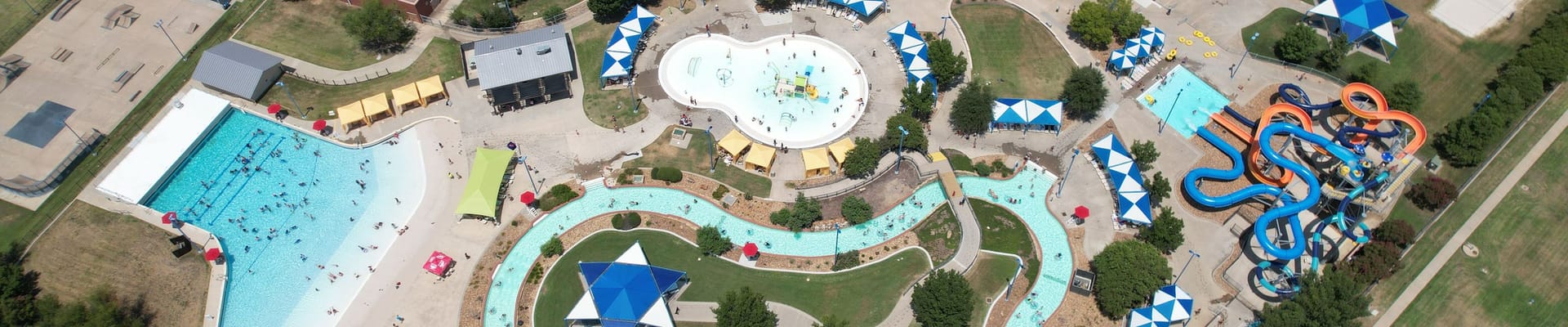 Water Works Park drone view with blue and orange slides, large wave pool with blue water, lazy river, and splash pad