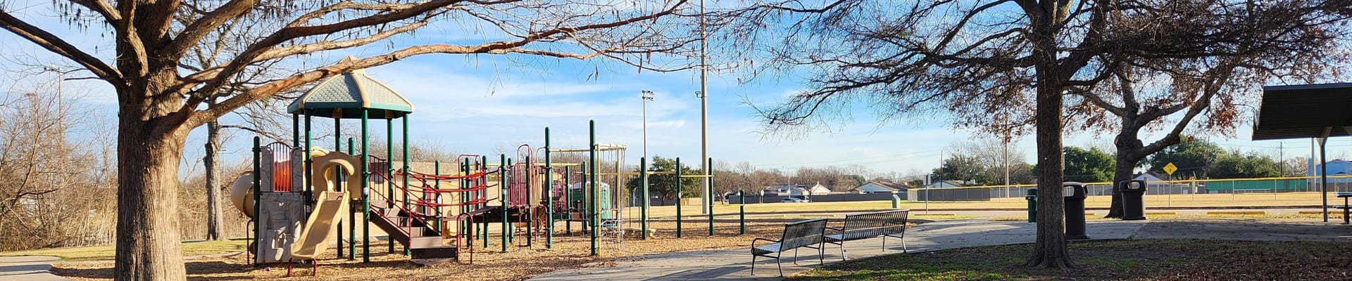 community park with playground equipment and ball fields surrounded by trees