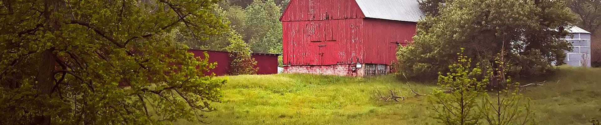 Red barn sitting on a hill overlooking a lake