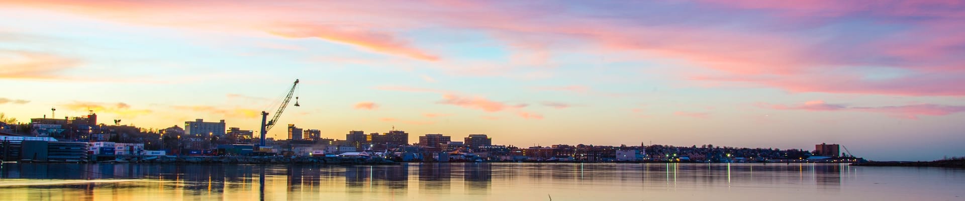 A view of Portland's harbor at sunset, with blue and pink clouds being reflected on the water's surface.