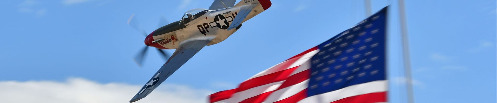 Plane from Air Races flying in the sky, as it passes the American Flag on bottom right