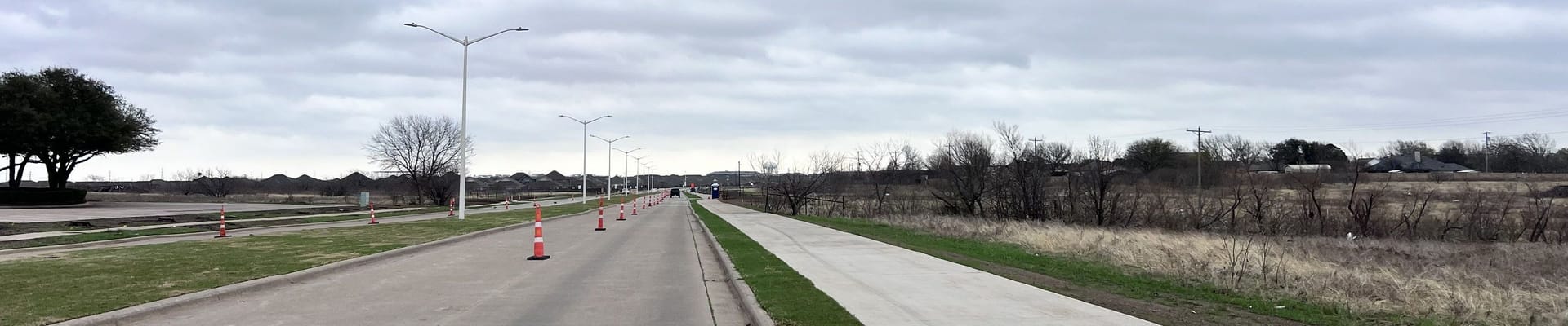 Photo of street with orange cones and green landscape with a sidewalk next to the street
