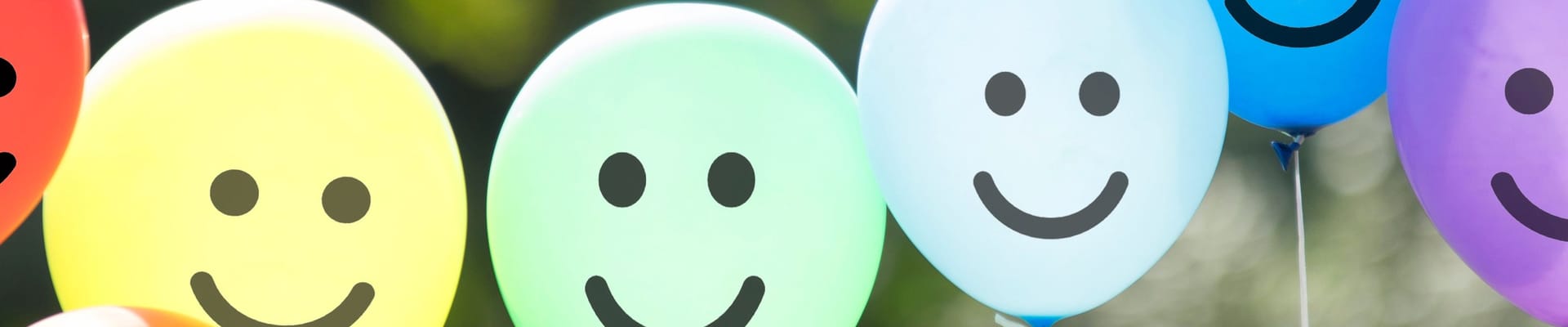 Seven colorful balloons with smiley faces. Starting from left to right - red, orange, yellow, green, blue, darker blue, and purple.