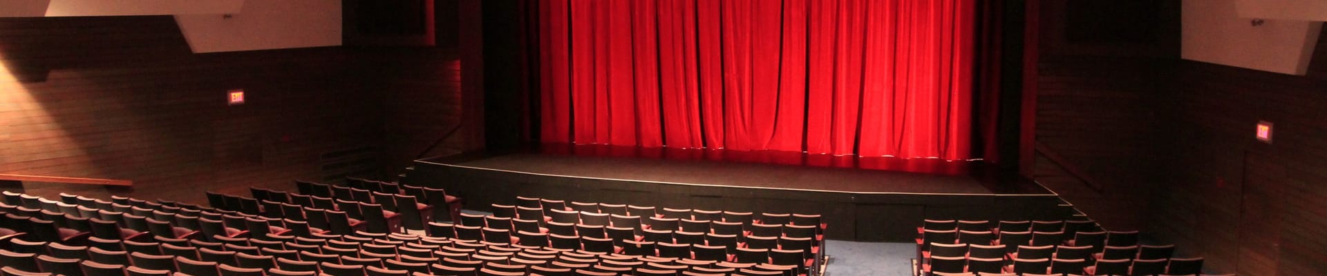 An indoor theatre with a raised stage and red velvet curtain.