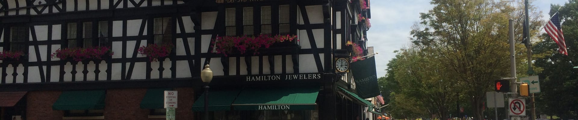 Brown and white building in downtown with people walking and car stopped.