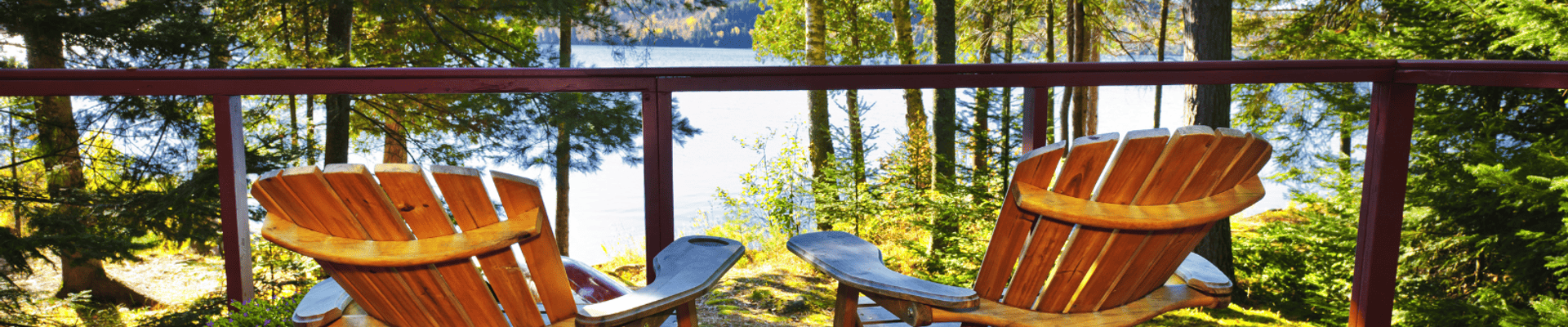 Photo of two muskoka chairs on a deck overlooking water through the trees.