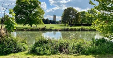 A view from the far side of Abbey lake looking across the water and lawn to see the Church Tower framed by trees.