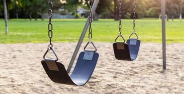 Playground for children with swings in the public park during sunset.