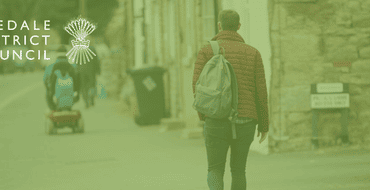 A man with a backpack and headphones on walking away from the camera along a leafy suburb street