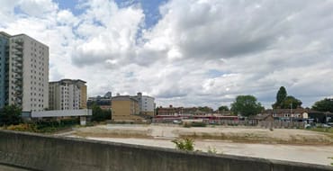 a large cleared development site beside the River Roding. Existing buildings and residential blocks surround the site, with open land in the foreground and a partly cloudy sky overhead. The image illustrates a significant redevelopment opportunity within the Ilford Opportunity Area.