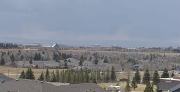 View across a Laramie residential neighborhood with homes, trees, an exposed hillside, and open landscape in the distance.