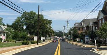 Picture of a road with businesses on either side and cars driving.