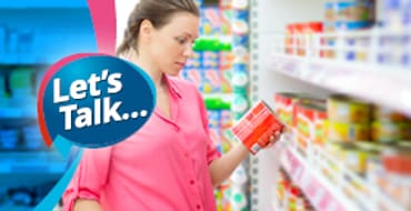 A lady looking at information on the back of a can of a food in a supermarket