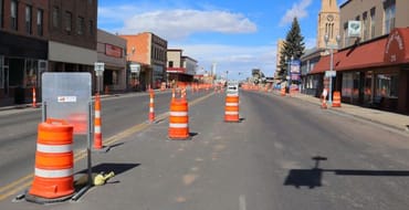 Downtown Laramie street undergoing construction, with traffic cones and barrels lining the roadway between storefronts.