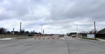 Street with orange cones and construction signage with gray sky