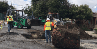 Construction workers and excavators digging up a paved residential street.