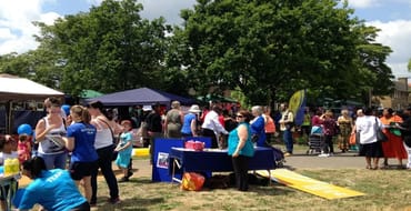 People at an outdoors event surrounded by stalls and trees