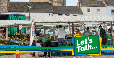 A photo of Richmond market traders setting up for market day with the 'Let's Talk...' branding of blue, green, yellow ribbons.