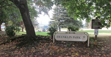 Franklin Park sign surrounded by trees with a playground in the background. 